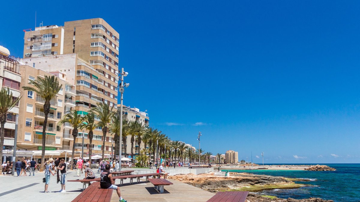 People strolling along the palm-lined Torrevieja seafront promenade on a sunny May day